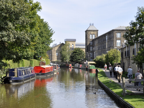 a canal with a series of boats on it and people walking beside the canal