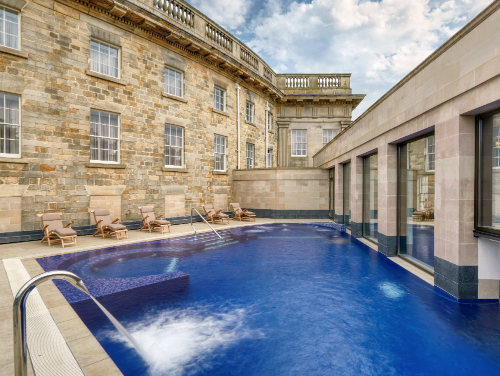 An empty outdoor pool at the back of a stone building with empty sun loungers at the side