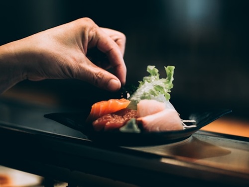 A hand decorating a plate of Japanese sushi
