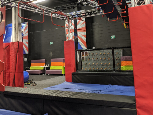 An indoor obstacle park with monkey bars up top and padding beneath.