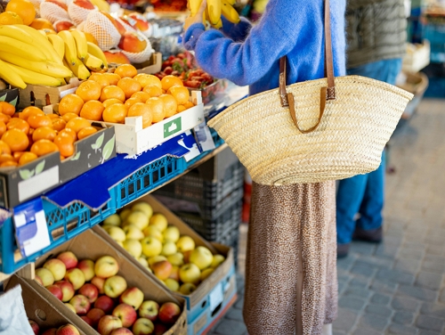 Woman with a big straw bag at a market stall selling fresh fruit
